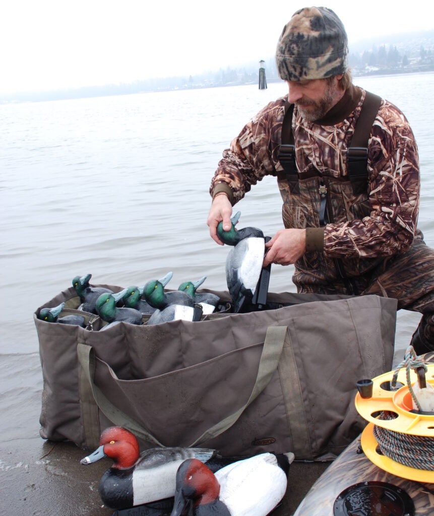 Hunter packing up diver duck decoys on the shore.