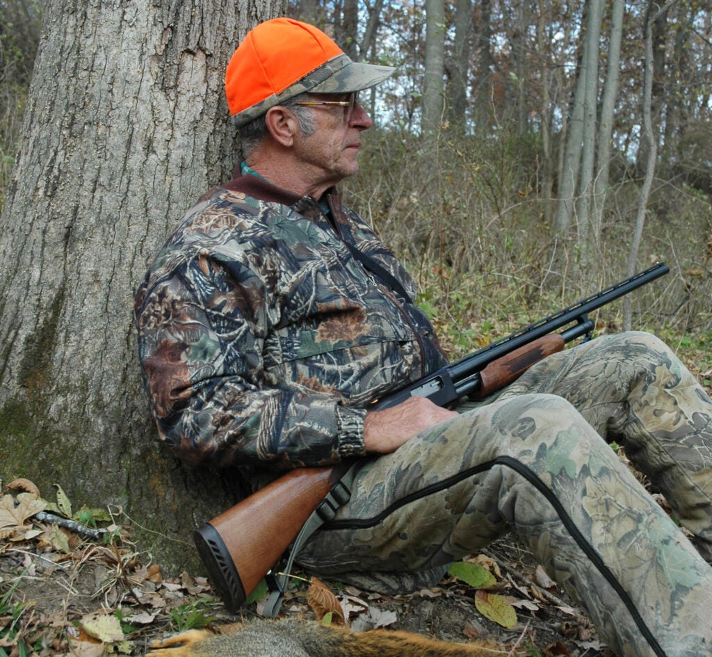Squirrel hunter with a shotgun sitting against a tree.
