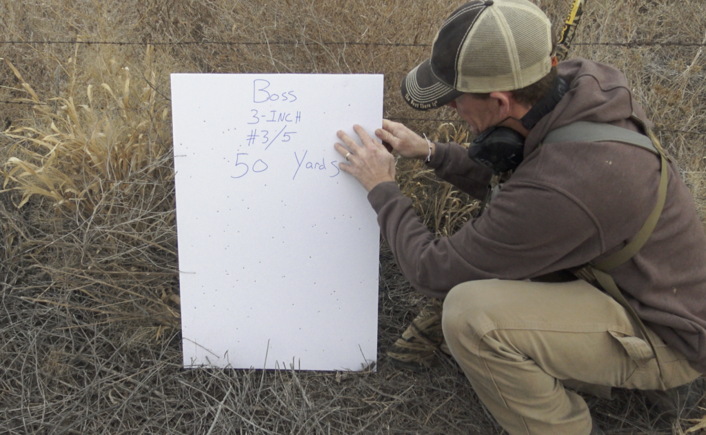 Man standing next to a shotgun patterning board counting pellet holes.