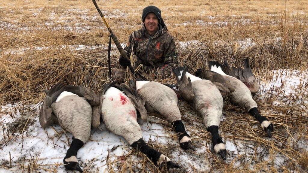 Goose hunter with five dead geese in a field.