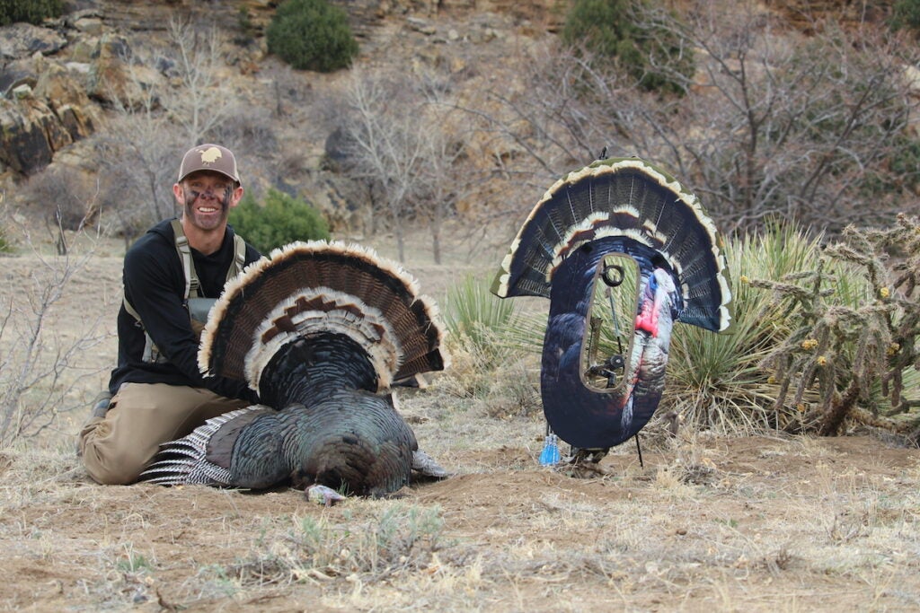 A turkey hunter with a dead turkey and a bow-mounted reaping decoy.