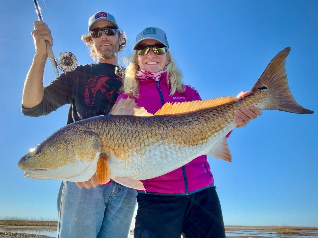 woman holds big redfish with man holding rod next to her