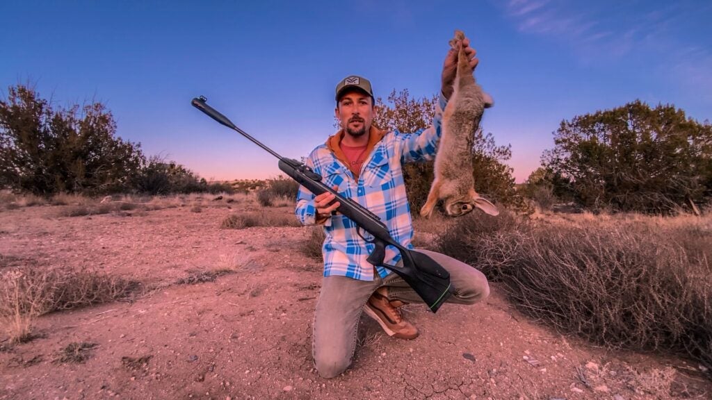 Hunter holding a dead rabbit and an airgun.