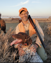 A hunter dressed in tan and orange hunting close knees beside a german shorthaired pointer
