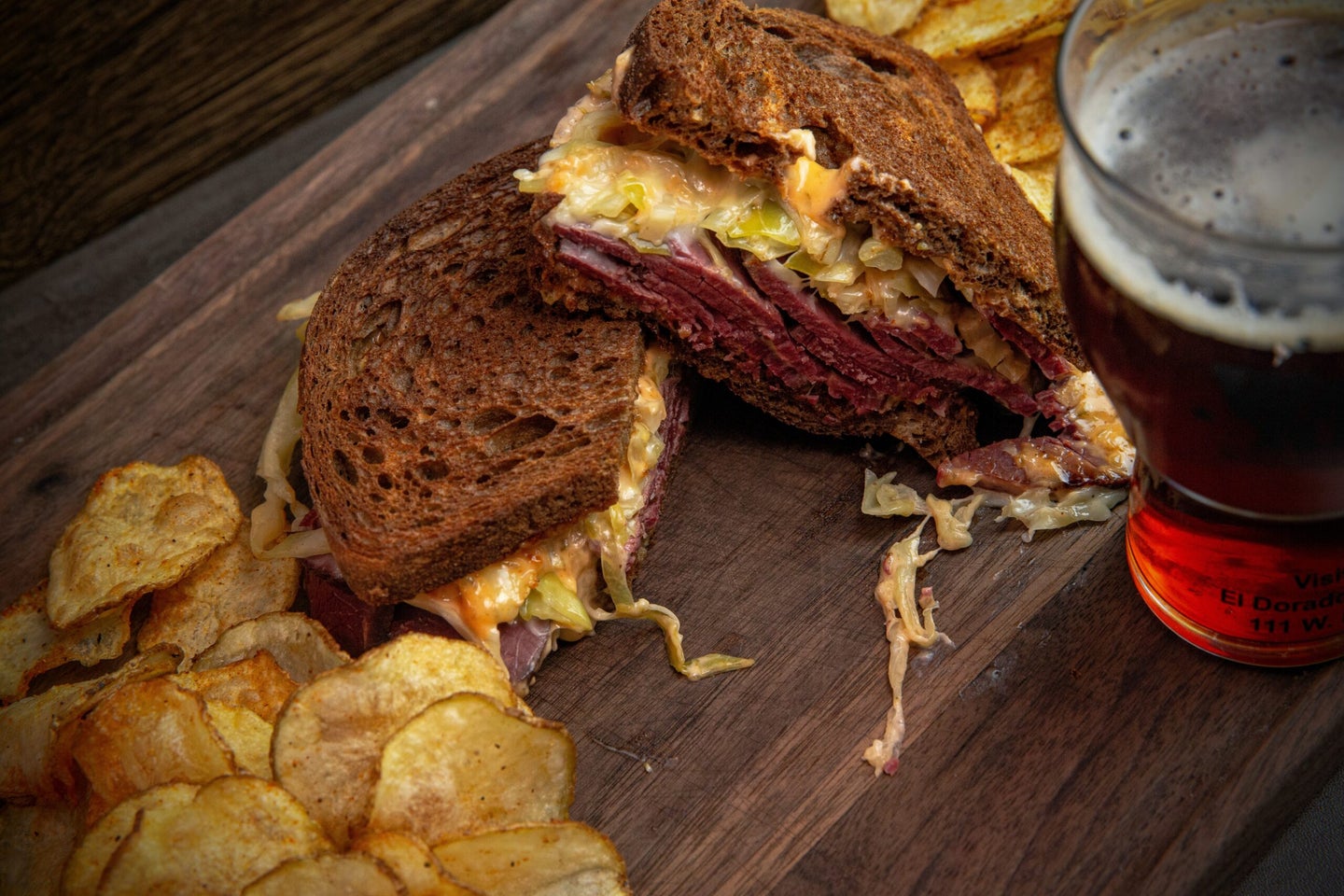 Venison Reuben on a cutting board with chips and a beer.