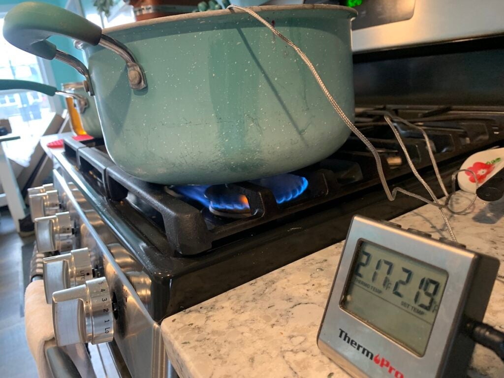 A pot on a stove with a thermometer sticking out of it.