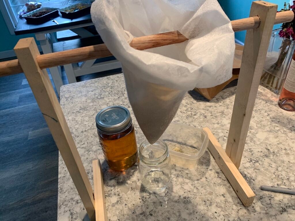 Maple syrup being filtered into a jar on a countertop.