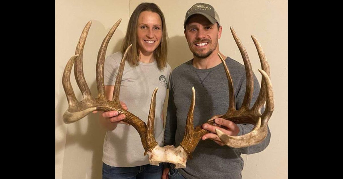 man and woman hold large rack of deer antlers