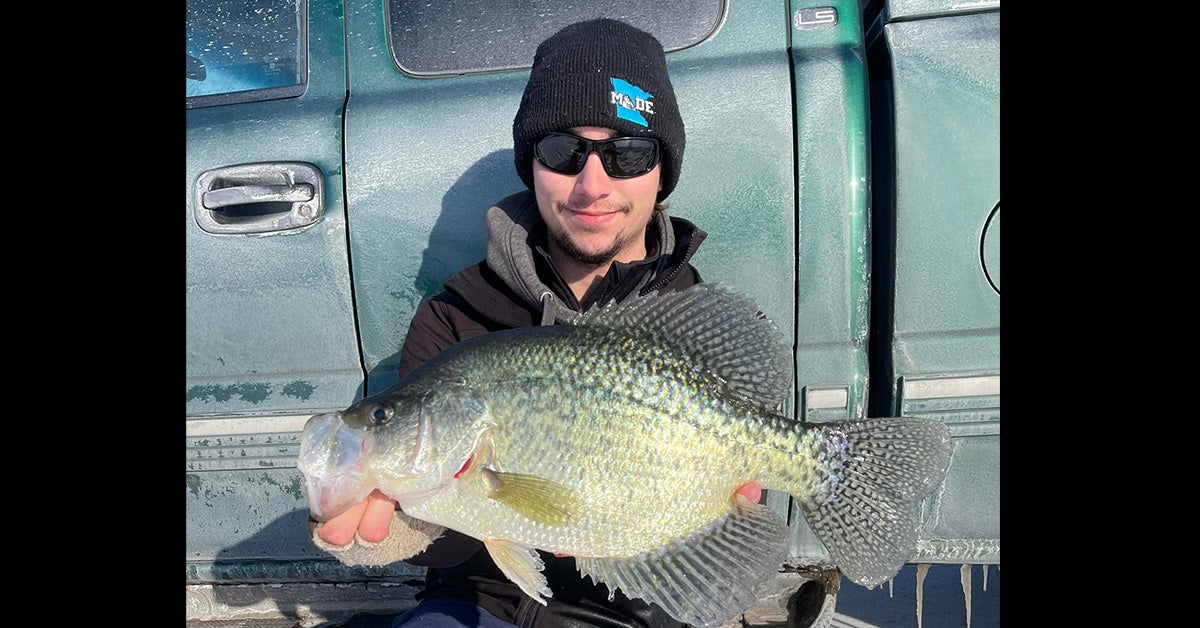 man holds crappie in front of vehicle
