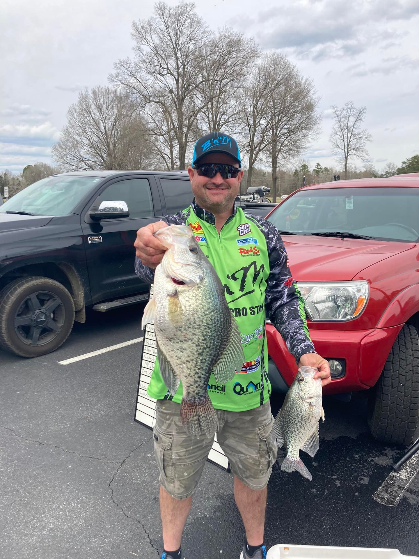 man holds large crappie in front of red pickup truck