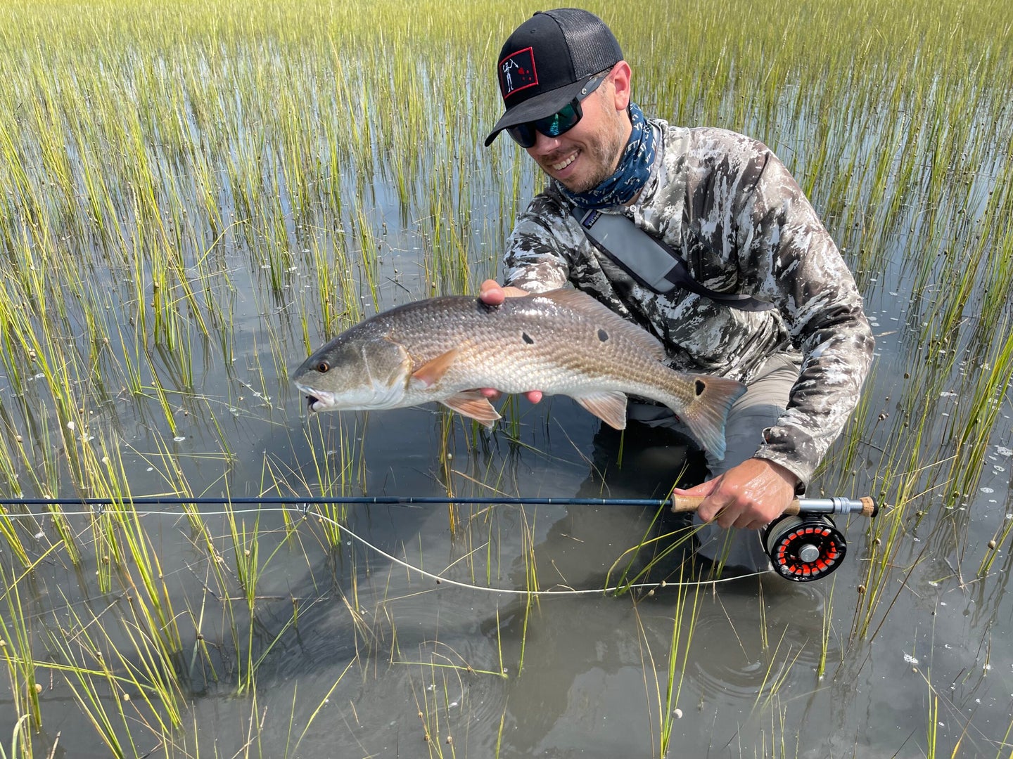 angler holds spotted redfish on salt marsh
