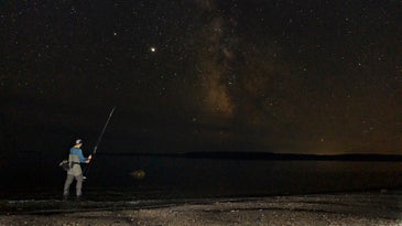 Striped bass angler fishing the shore under a full moon.