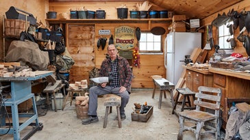 Decoy carver J.P. Hand sitting at a bench in his workshop.