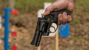 Hand holding a revolver at a shooting range.