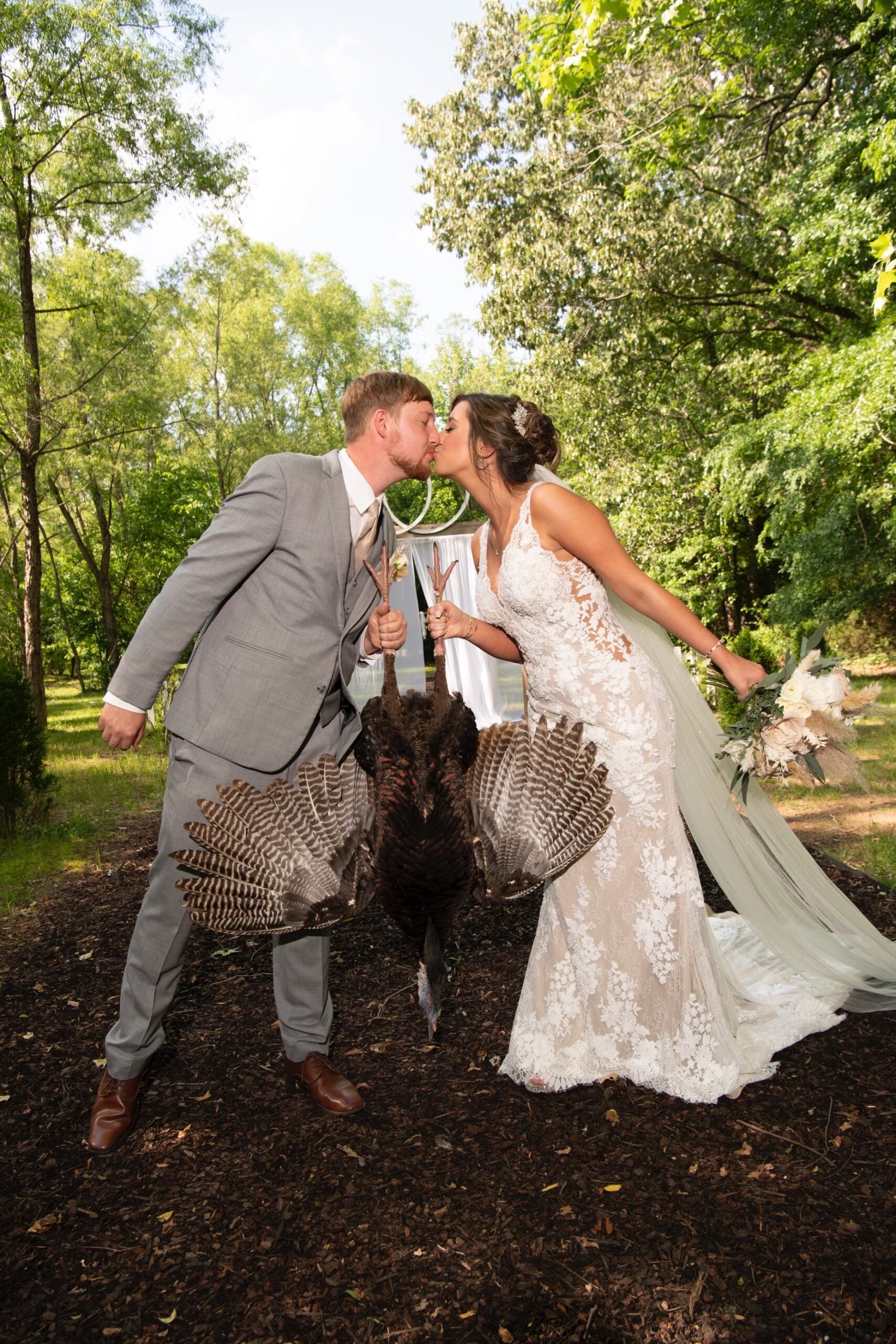 bride and groom kiss while holding dead wild turkey