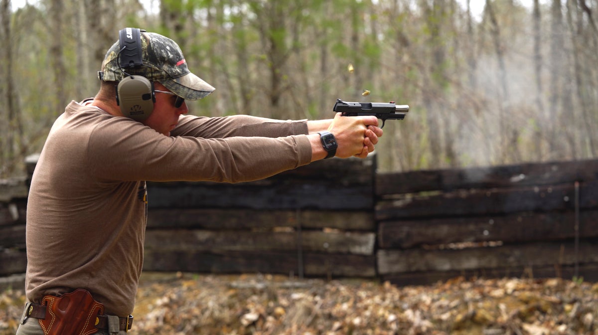 Man shooting a handgun in the woods.
