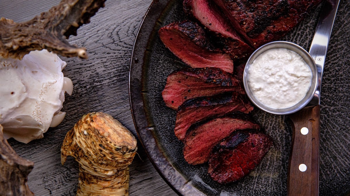 Cooked venison backstrap on a plate with a knife and horseradish sauce.