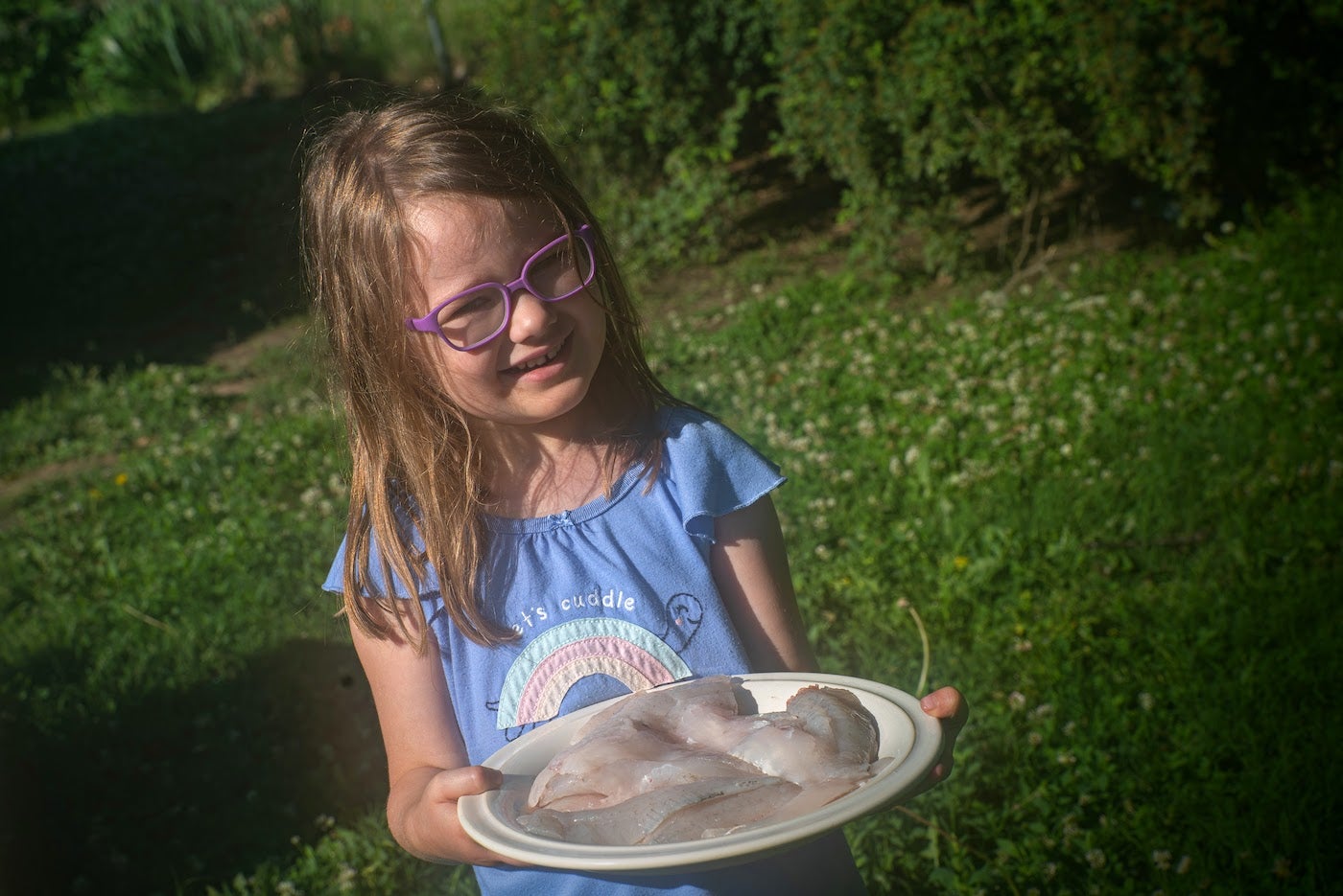 child holding a plate of fish fillets.