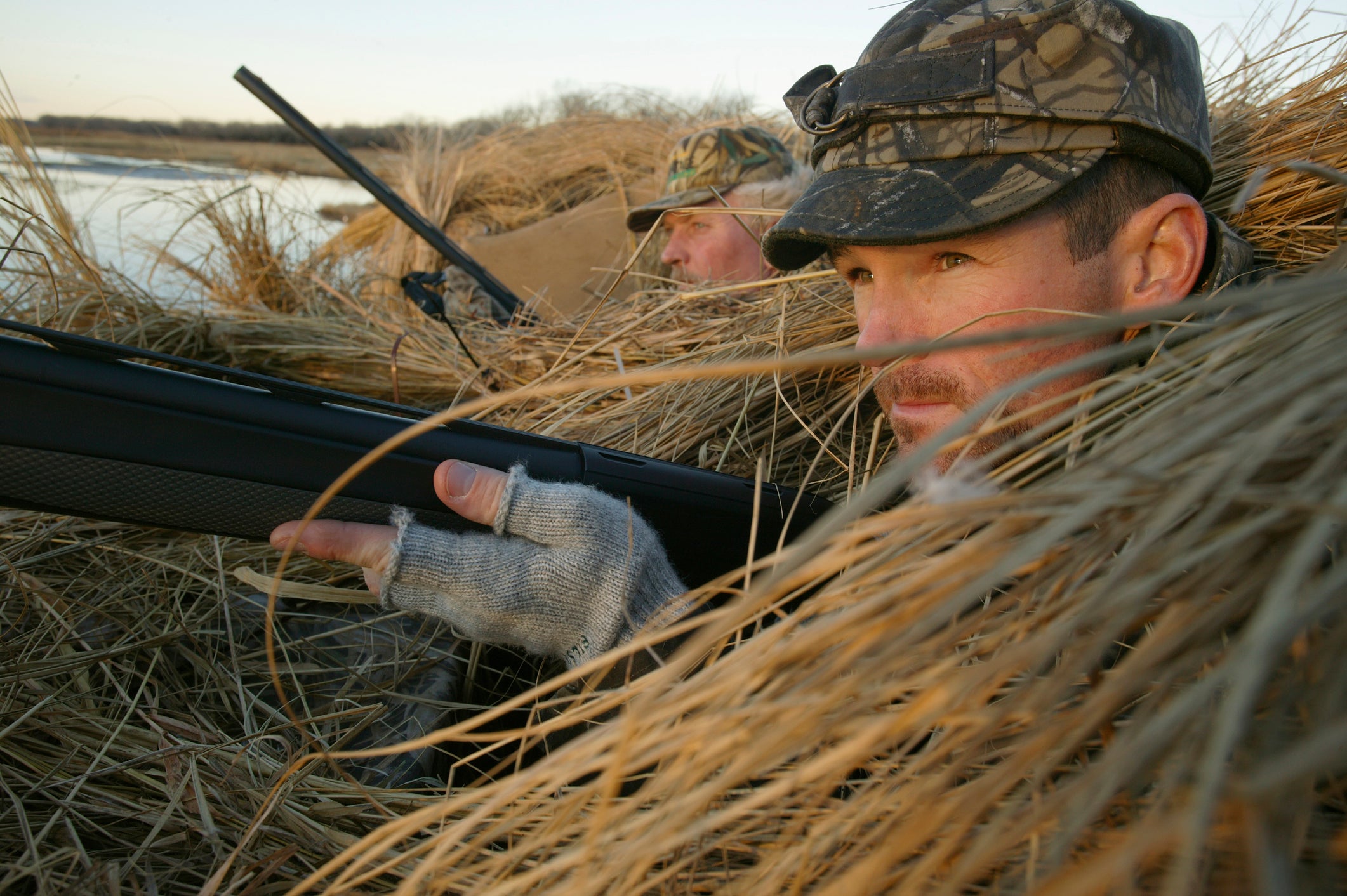 Duck hunter peering out of a blind covered in grass.