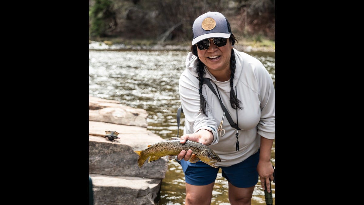 woman holds brown trout in front of river