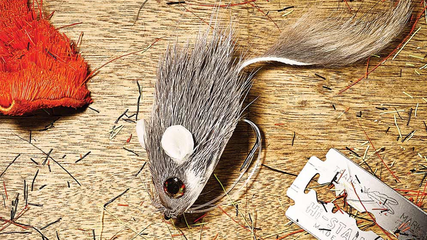 A deer-hair mouse fly lying on a table with hair shavings and a razor blade.