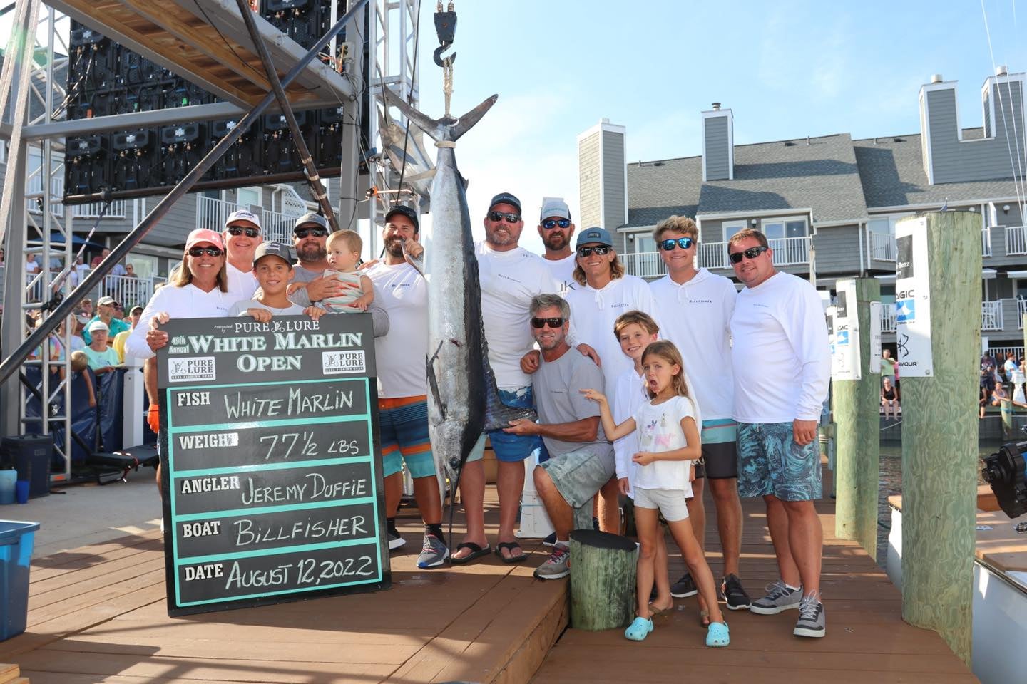 people gather around white marlin on scale