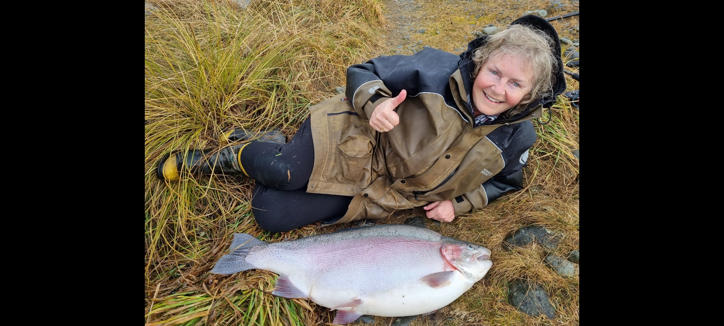 the woman lies on the ground next to the large rainbow trout