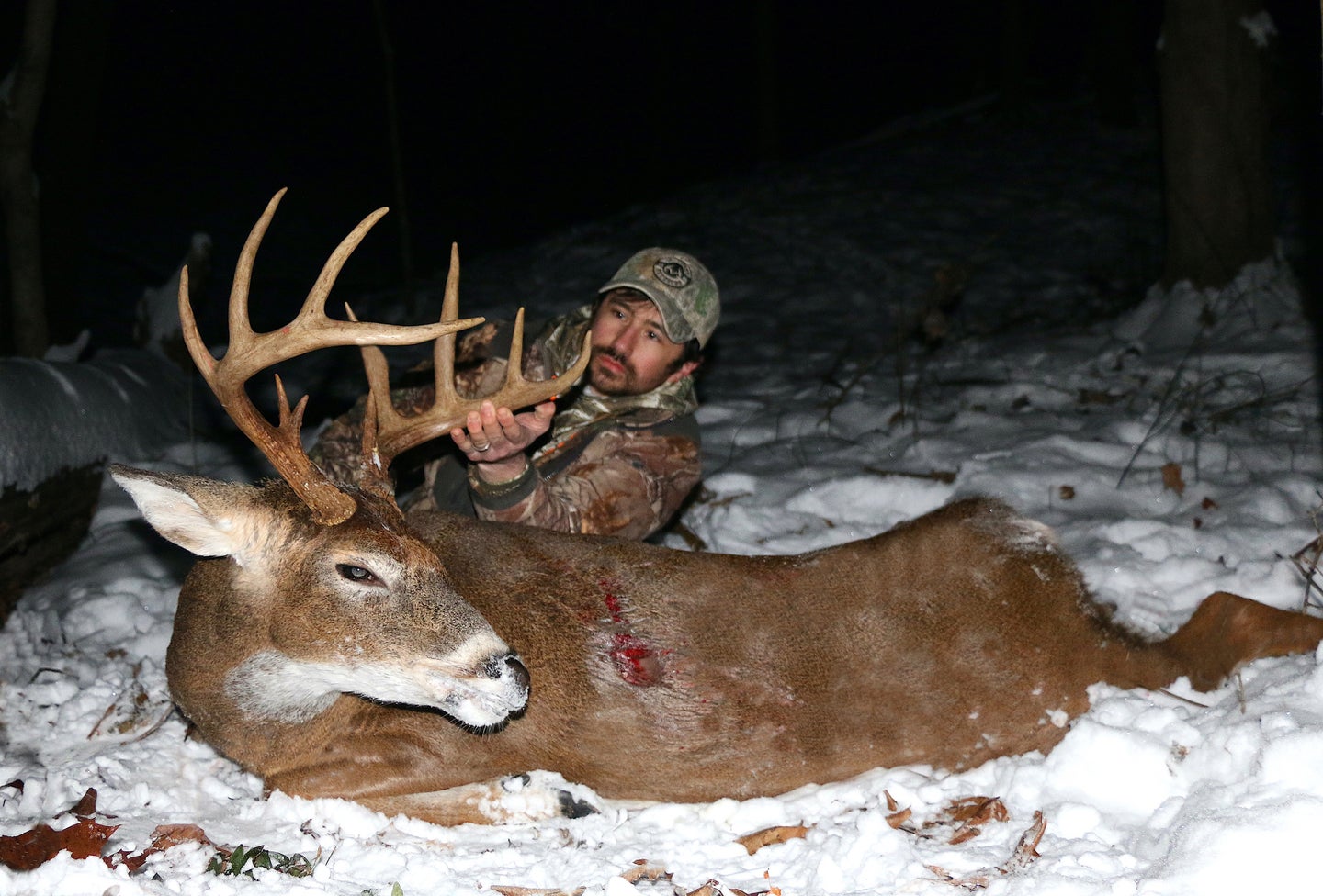 hunter laying in the snow with a dead whitetail deer.