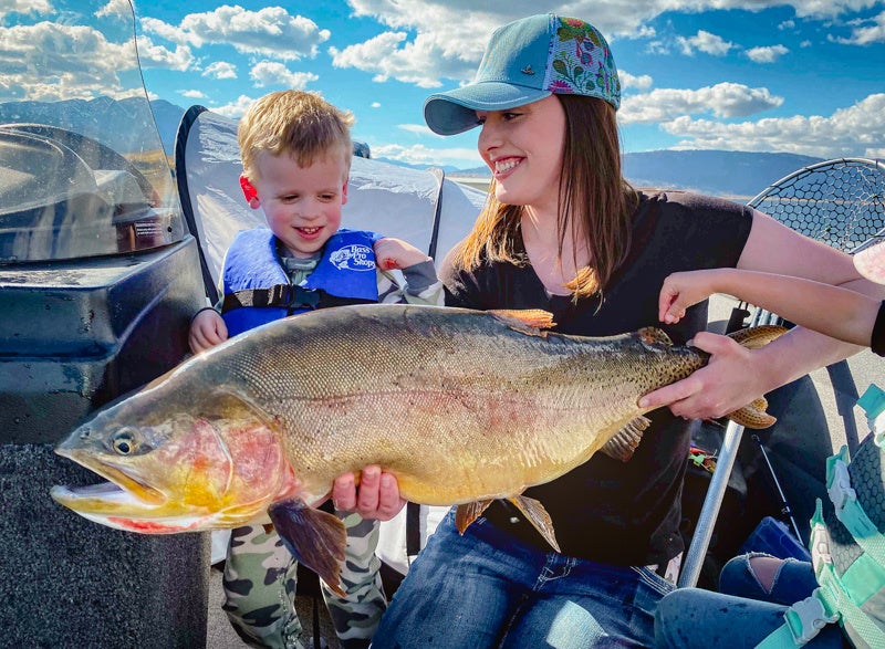 woman holds big trout with son on boat