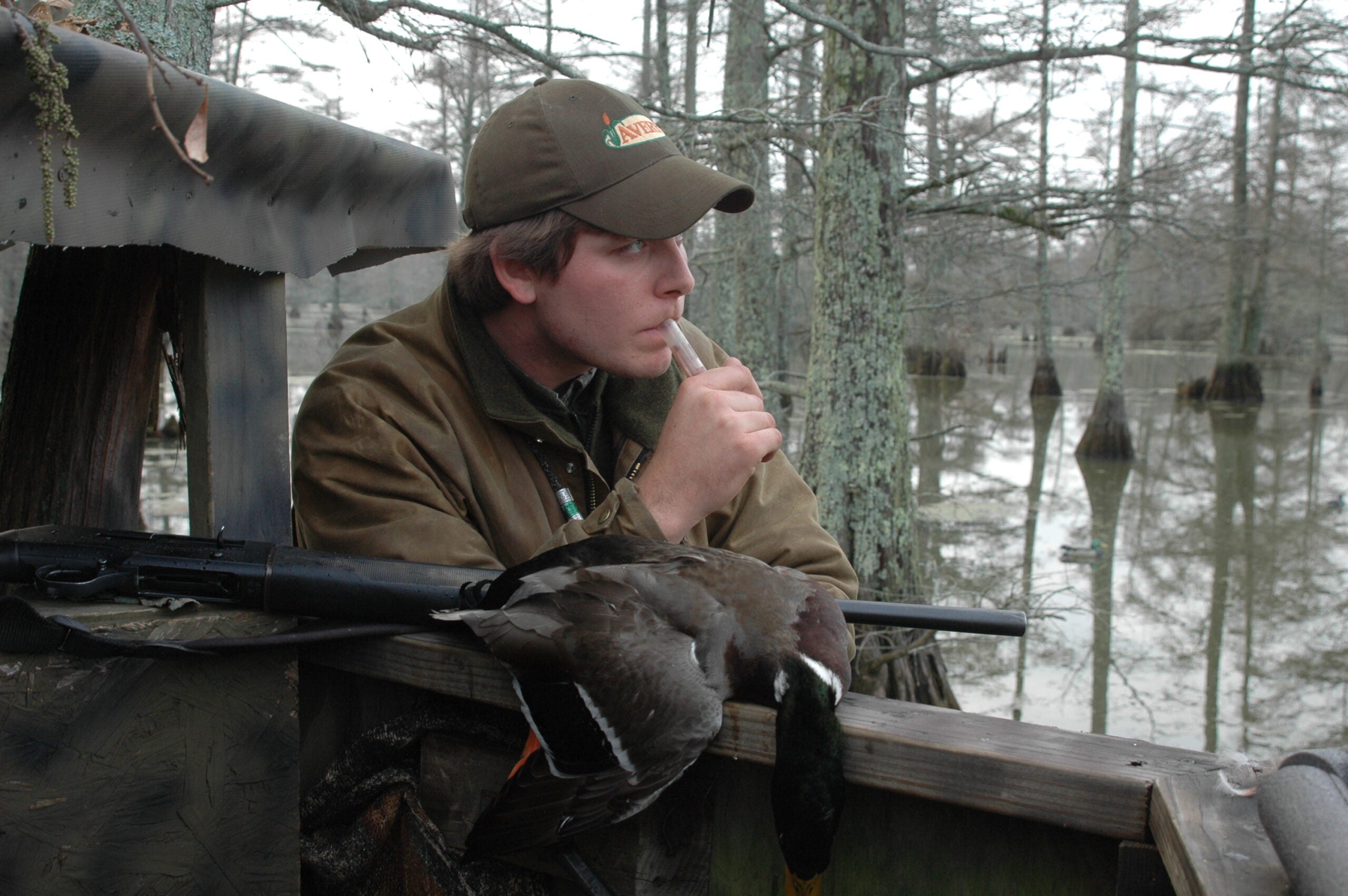 A man calls a duck decoy while standing next to a boat.