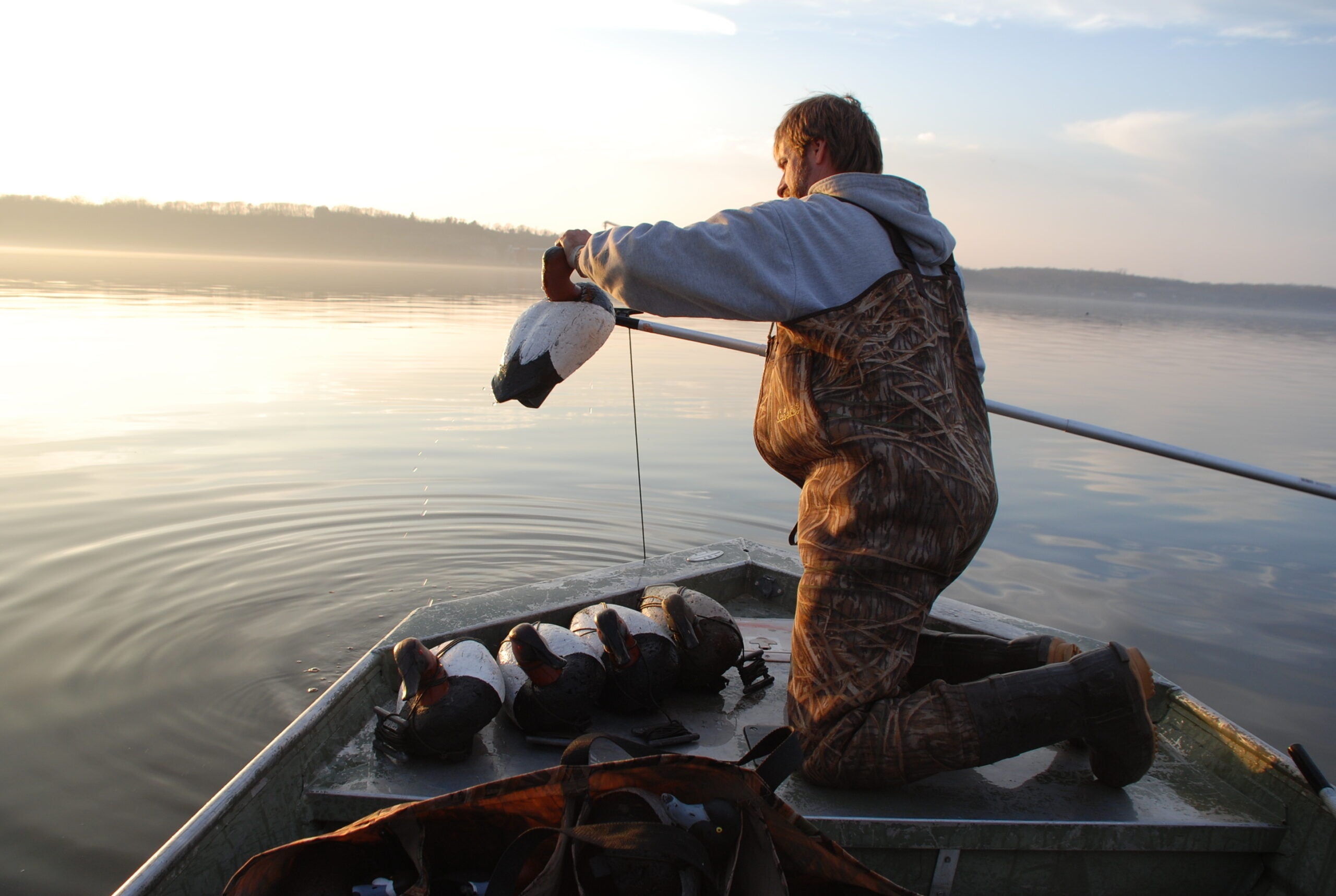 Man throwing duck decoys into the water from a boat.