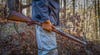 Man holding a hunting rifle in the woods.