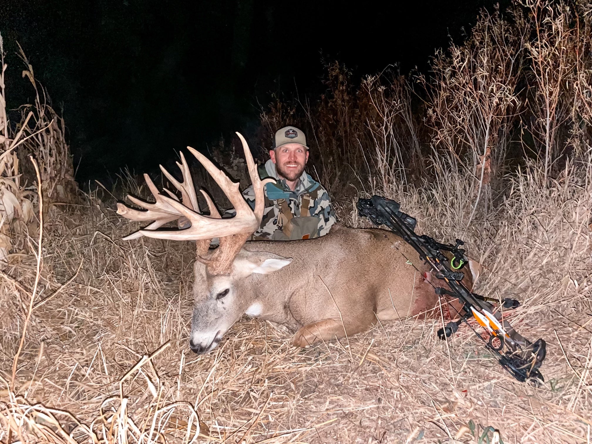 man poses with large whitetail deer buck and bow