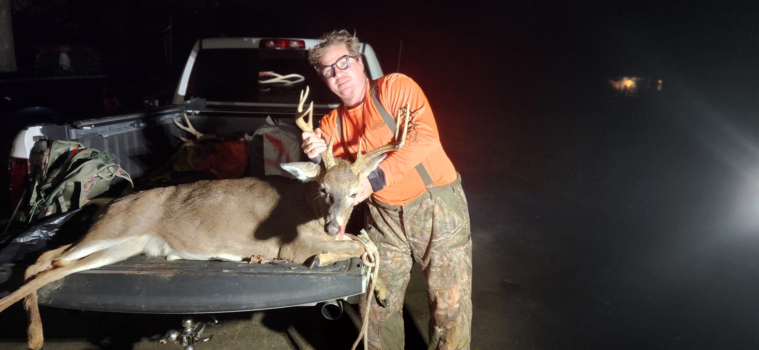 hunter holds head of antlered deer behind pickup truck