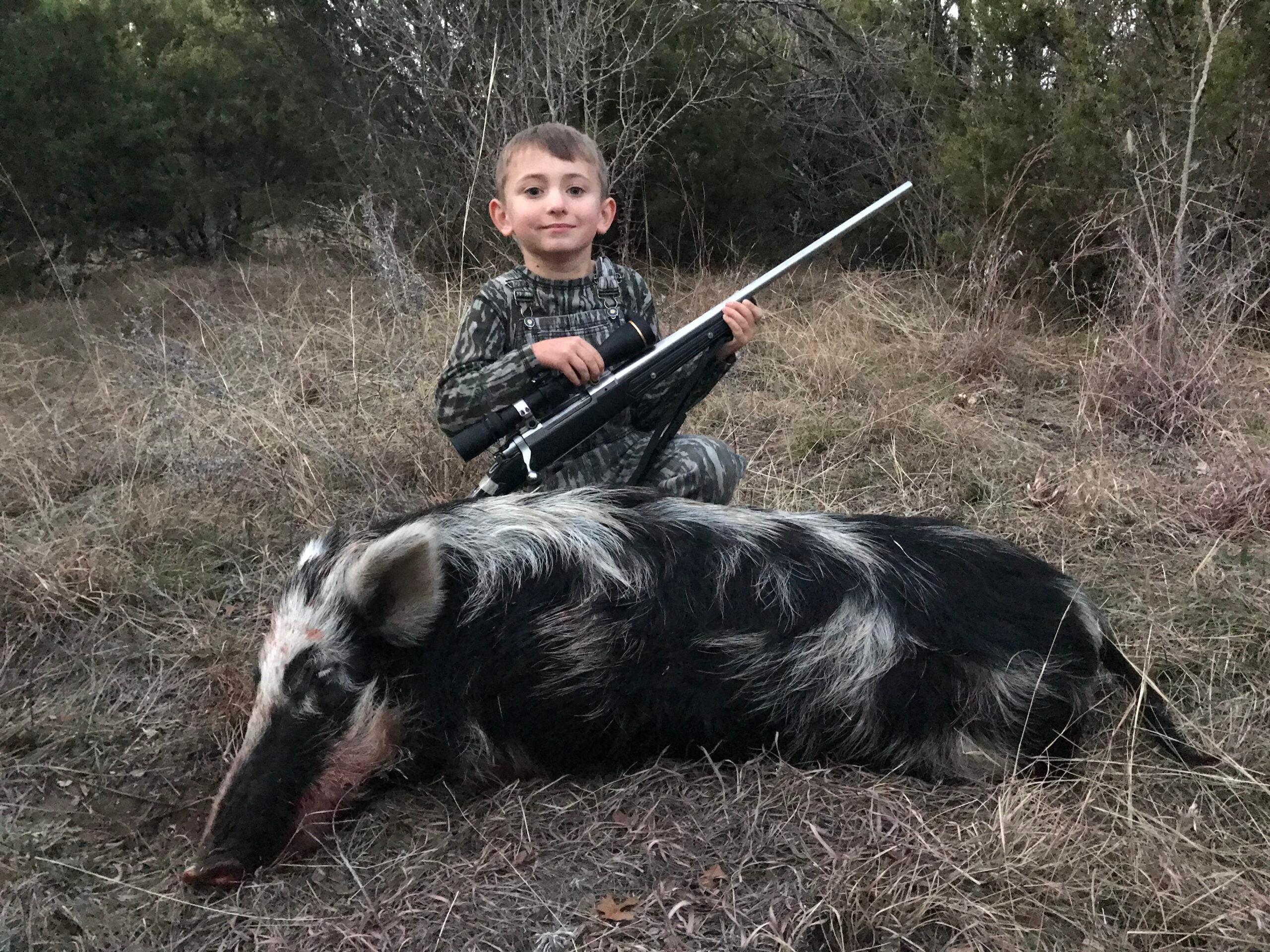 Boy with a rifle sitting next to a dead hog.