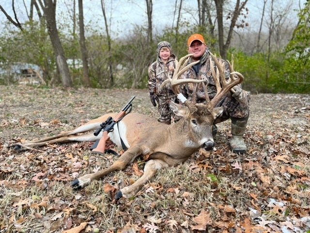 deer hunter and son pose with large buck