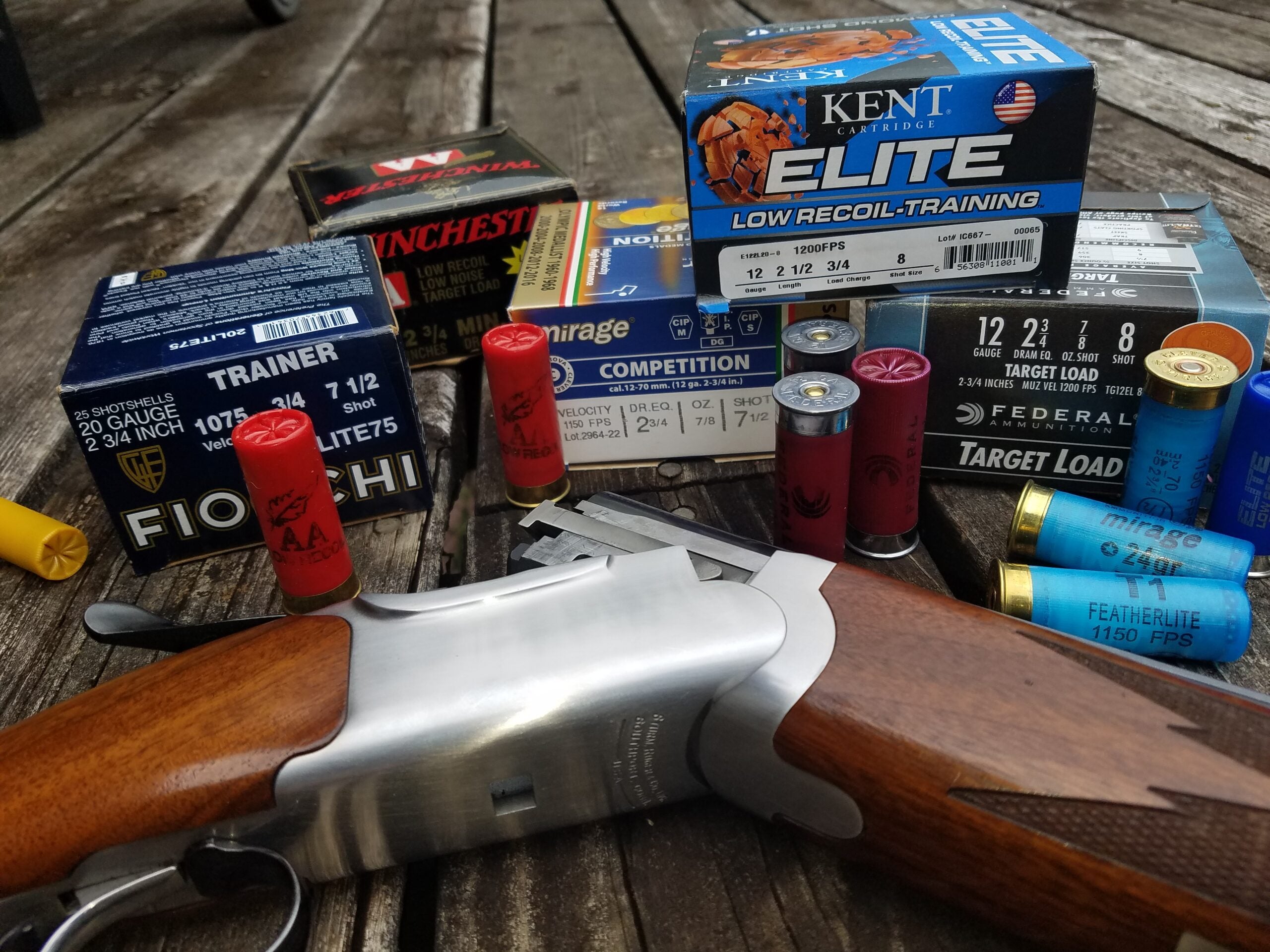 Different types of shotgun shells on a table with a shotgun.
