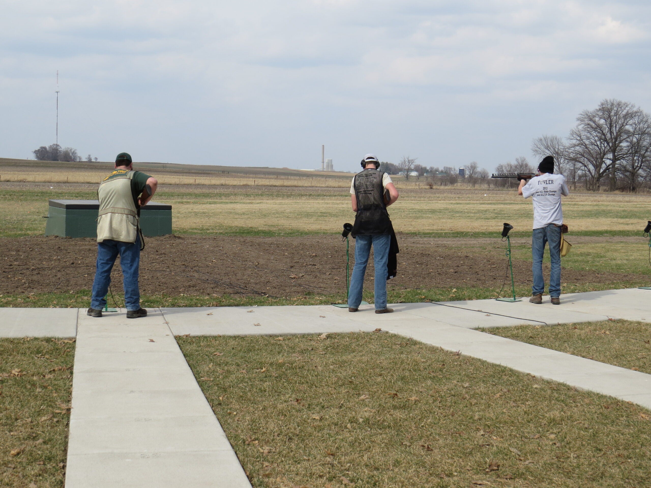 three trap shooters stand at the ready.