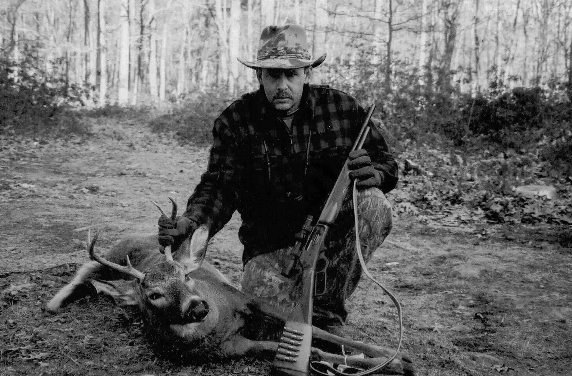Hunter next to a dead deer with a lever-action rifle in his hand.