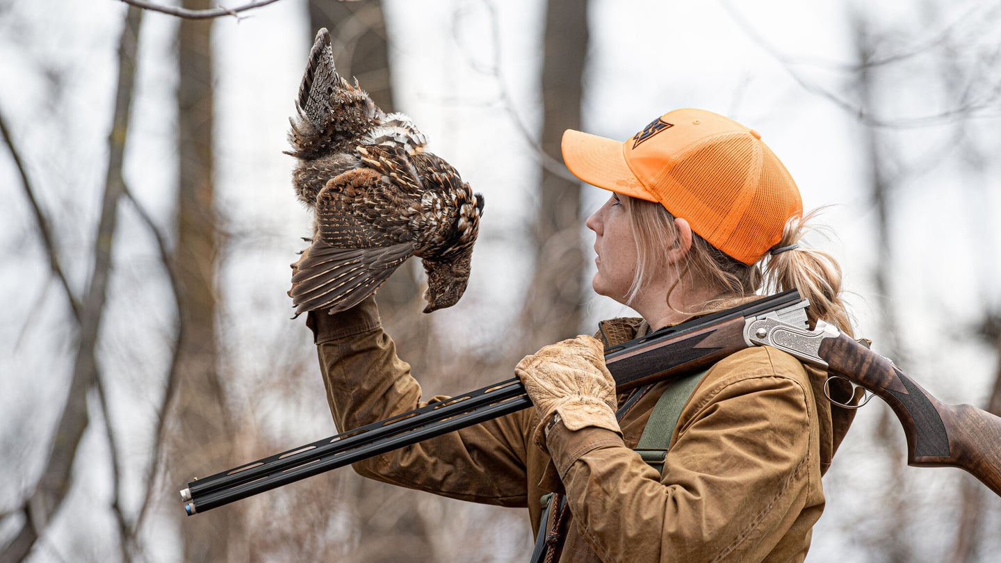 Upland hunting woman holding dead ruffed grouse.