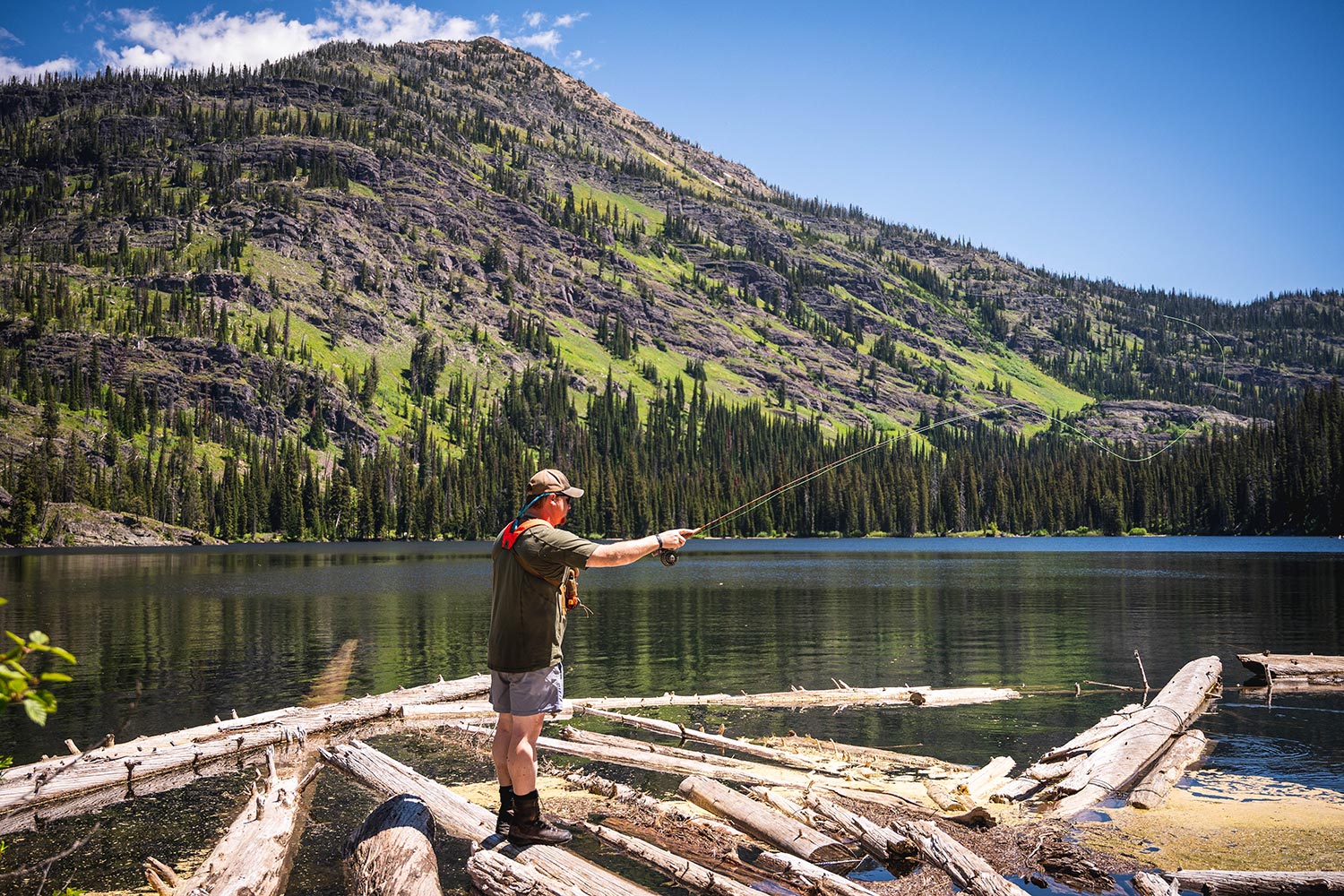 Angler fly casts from logjam into placid mountain lake