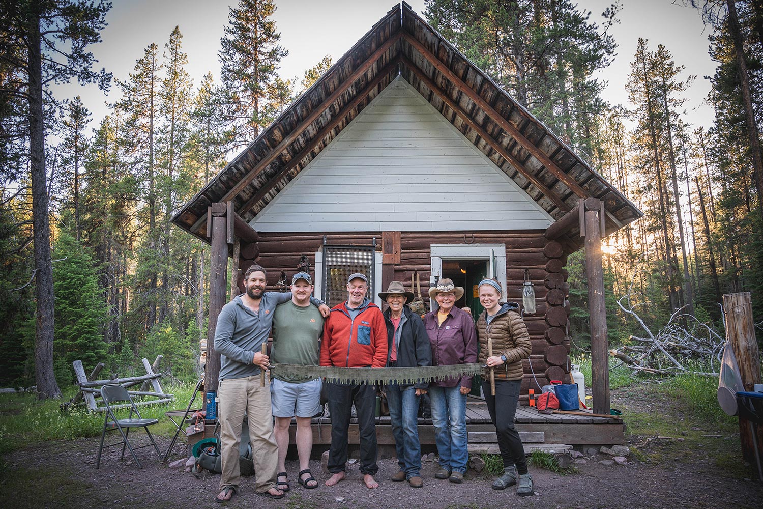 Group with crosscut saw poses outside cabin