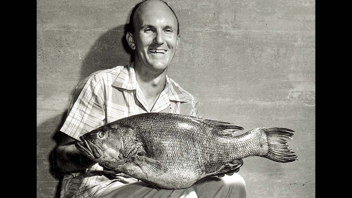 man poses with large smallmouth bass in black-and-white photo