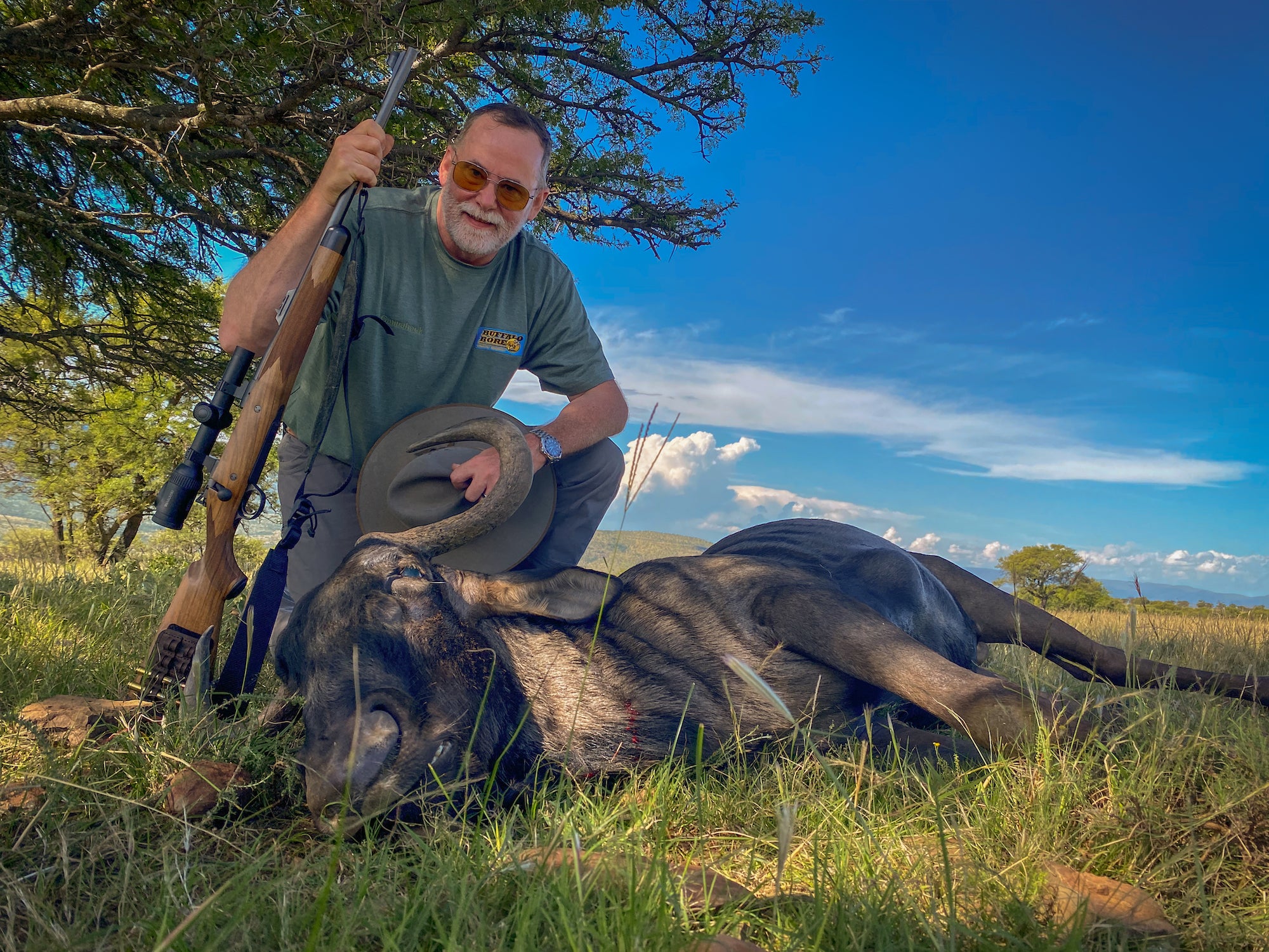 Man with a dead wildebeest holding a rifle.