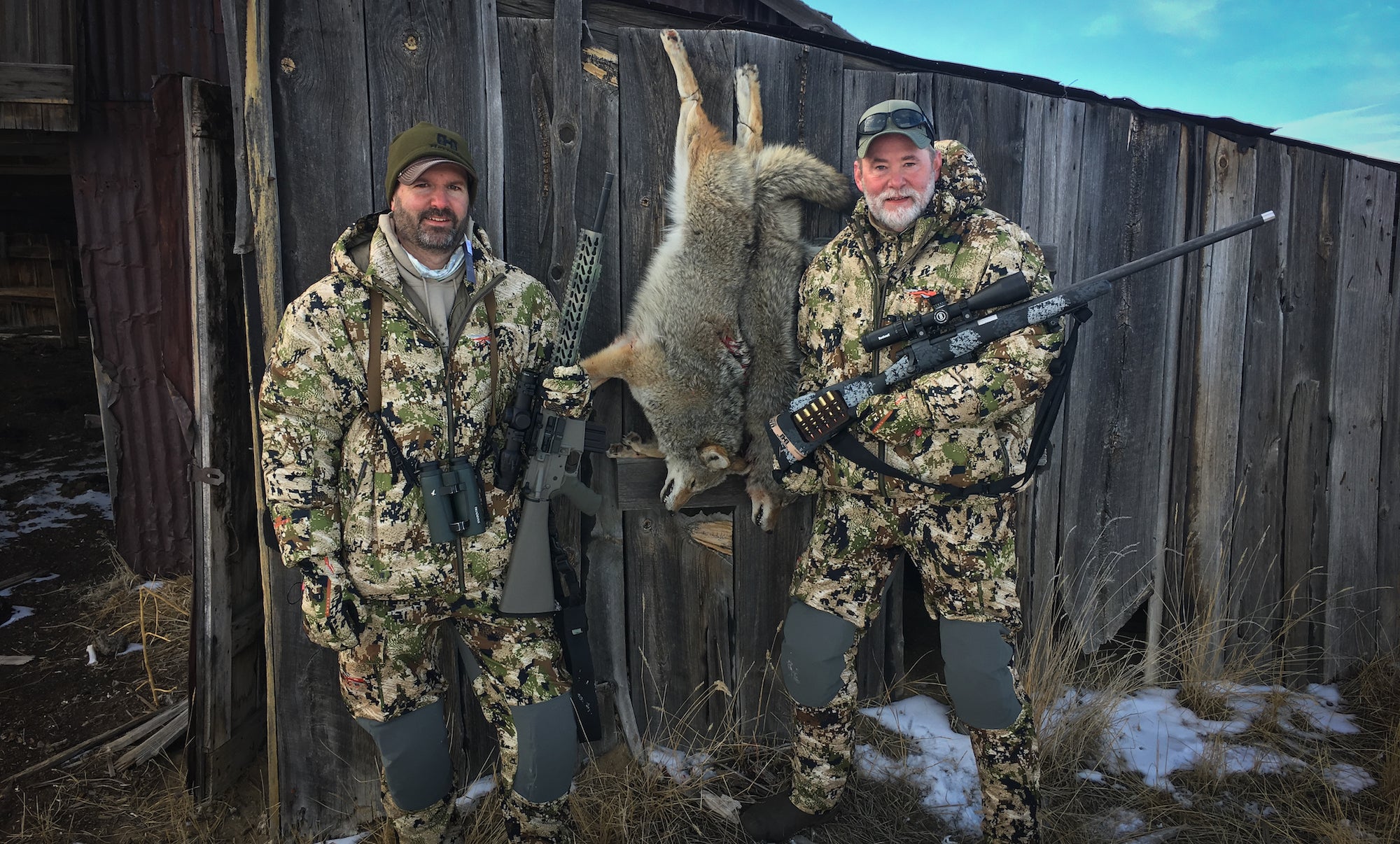 Two men with rifles standing next to dead coyotes.