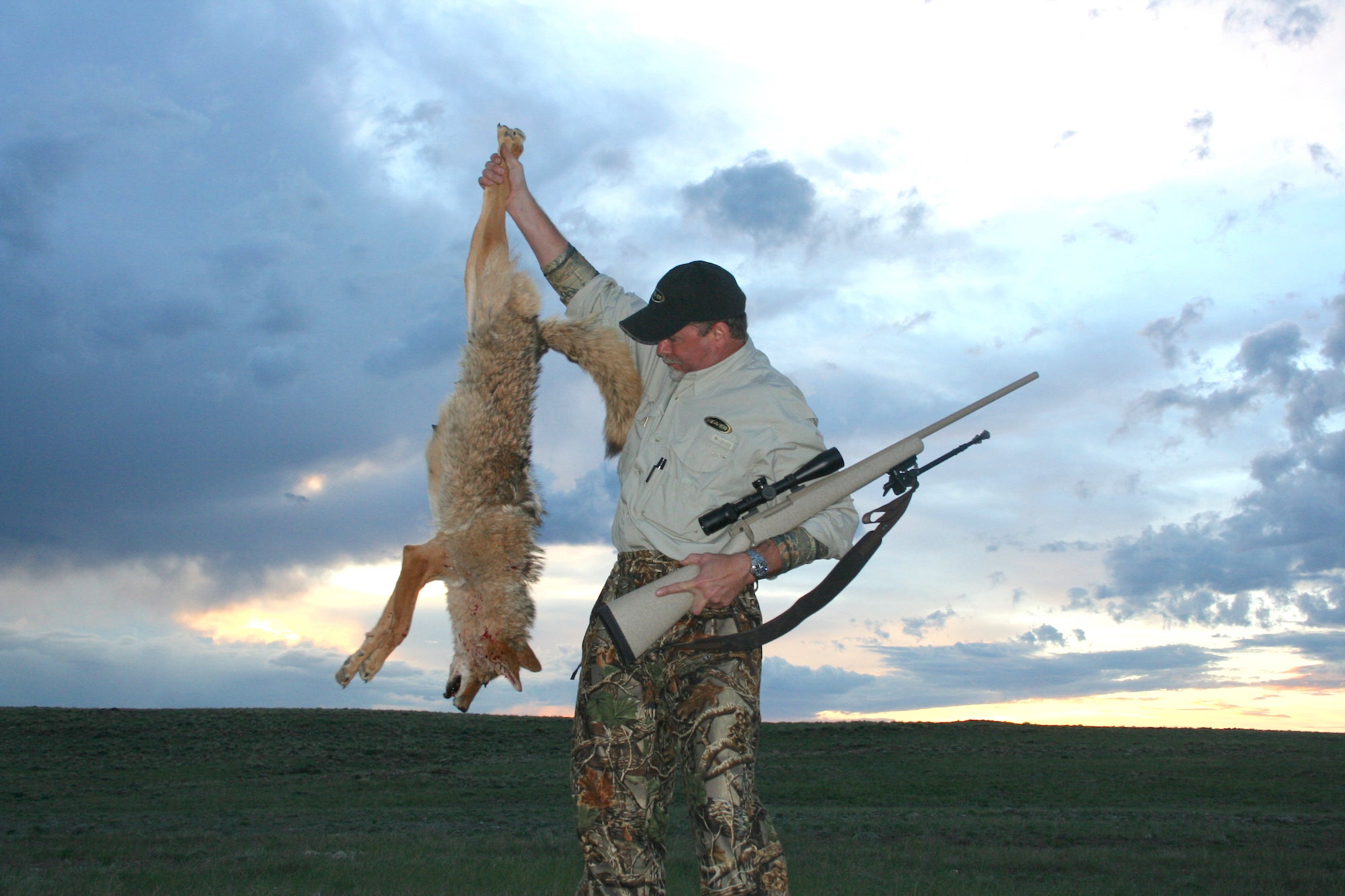 Man holding a coyote and a rifle.