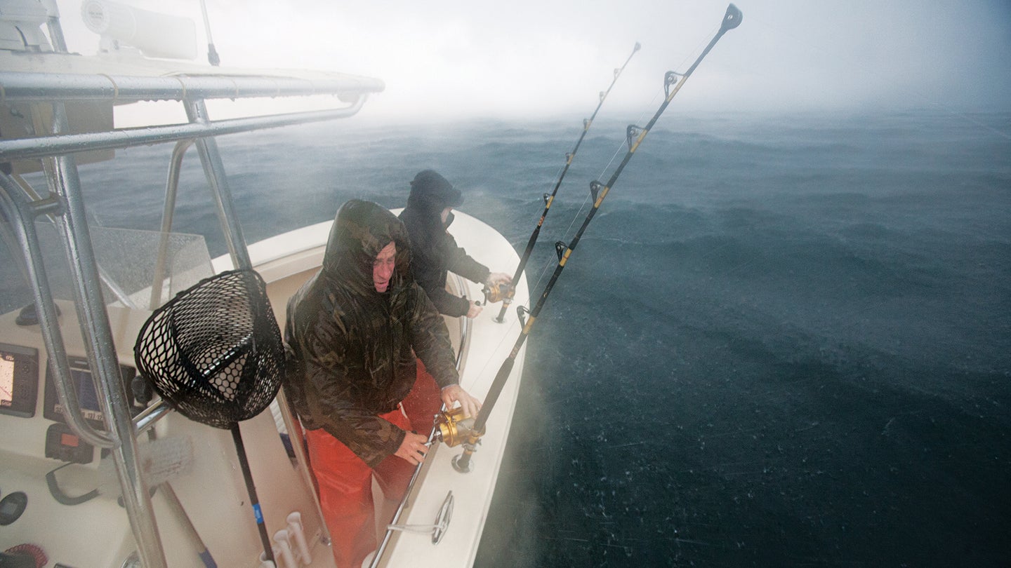 Two fishermen watch fishing rods at bow of boat in foggy, wet weather