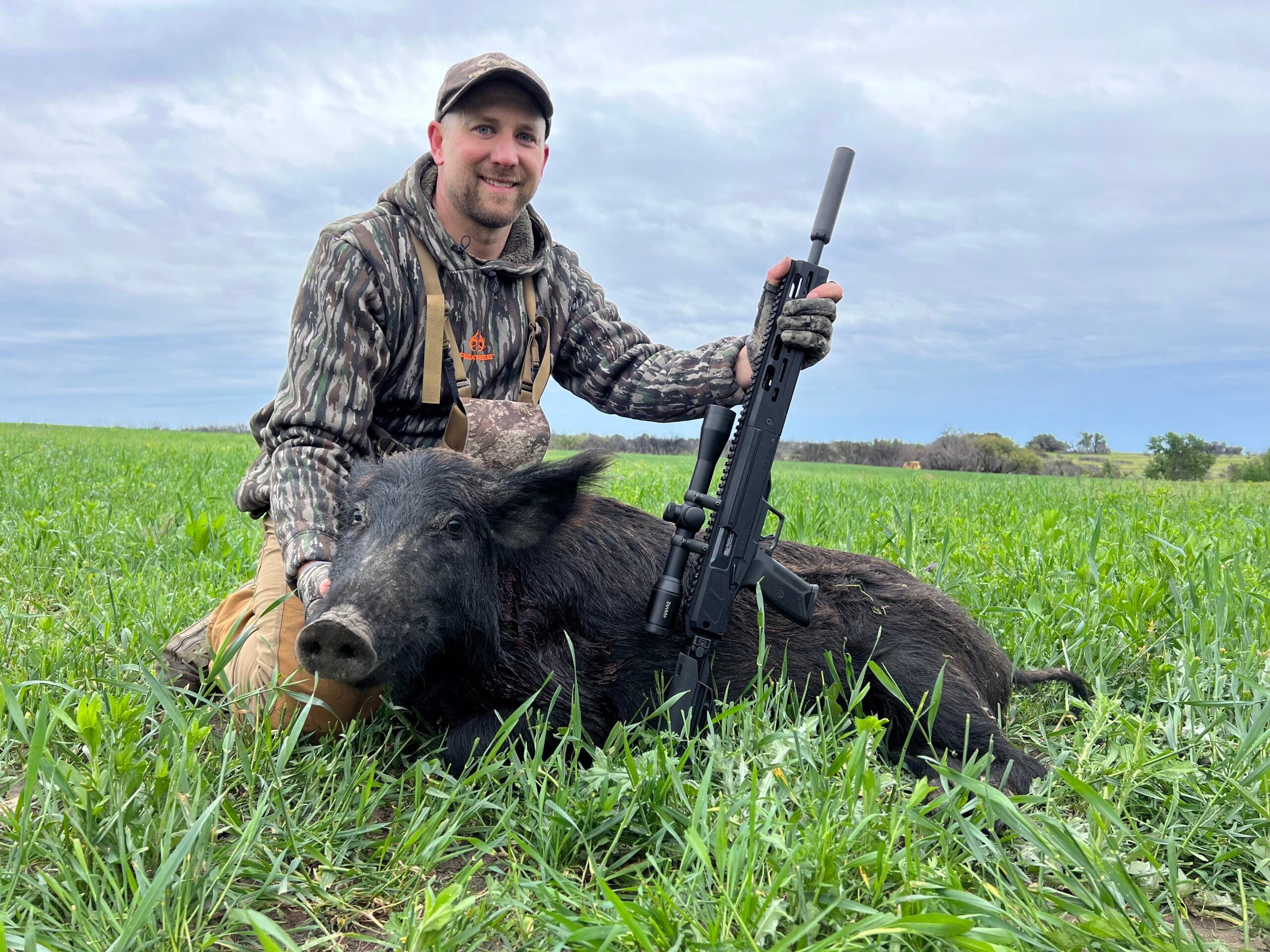 Man with a rifle sitting next to a dead pig.
