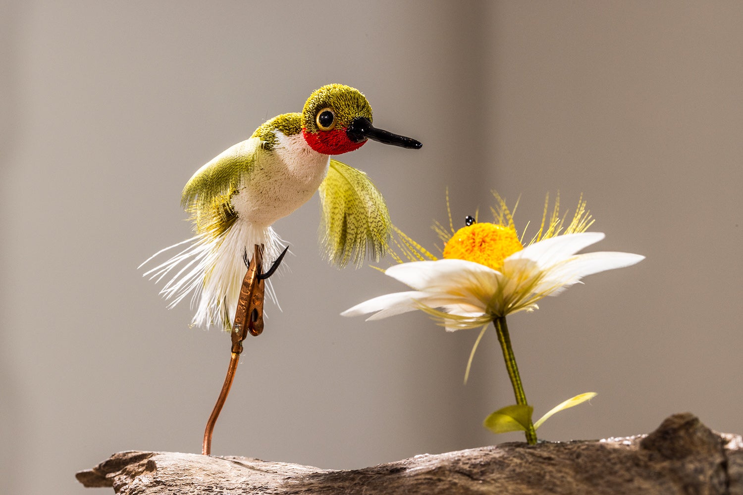 deer-hair hummingbird sculpture hovers over daisy