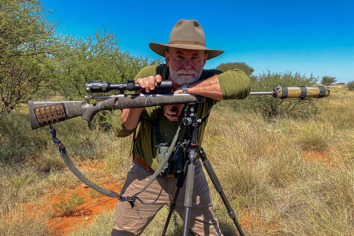 hunter leans on gun on tripod